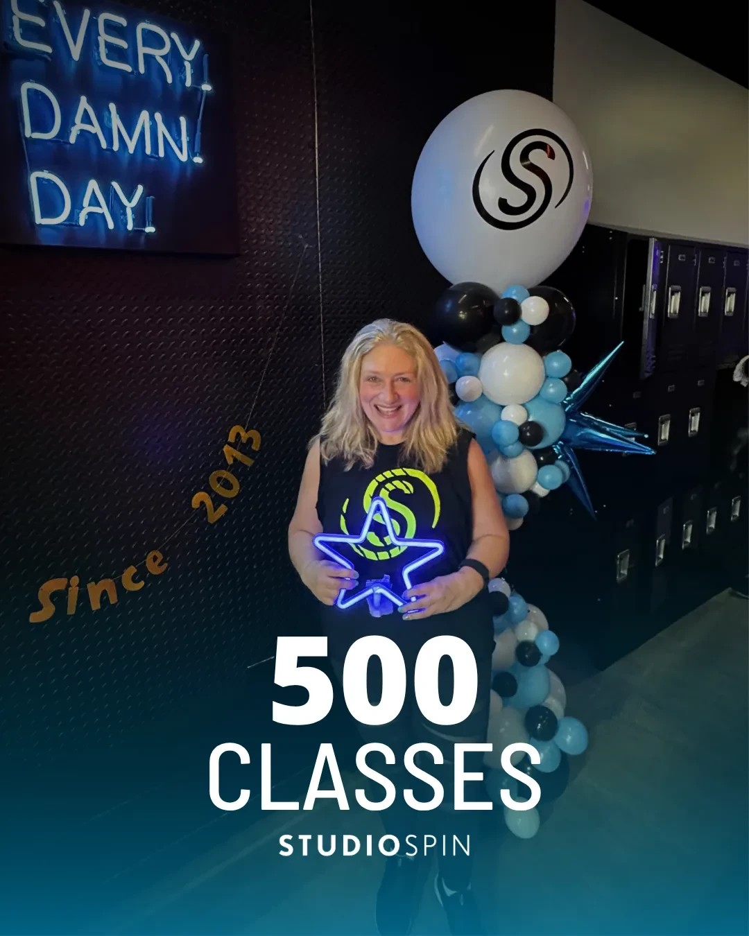 A Studio Spin member celebrating 500 classes under the Every Damn Day neon sign.