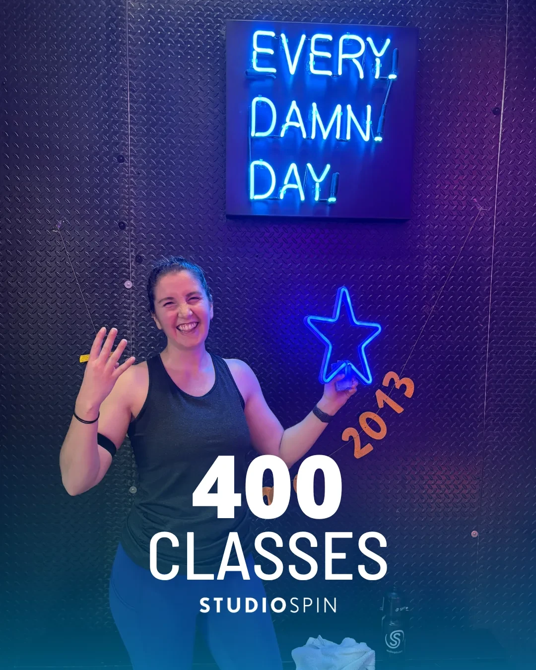 A Studio Spin member celebrating 400 classes under the Every Damn Day neon sign.
