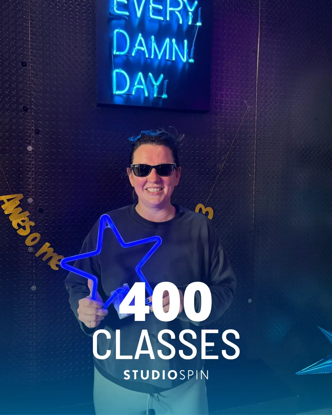 A Studio Spin member celebrating 400 classes under the Every Damn Day neon sign.
