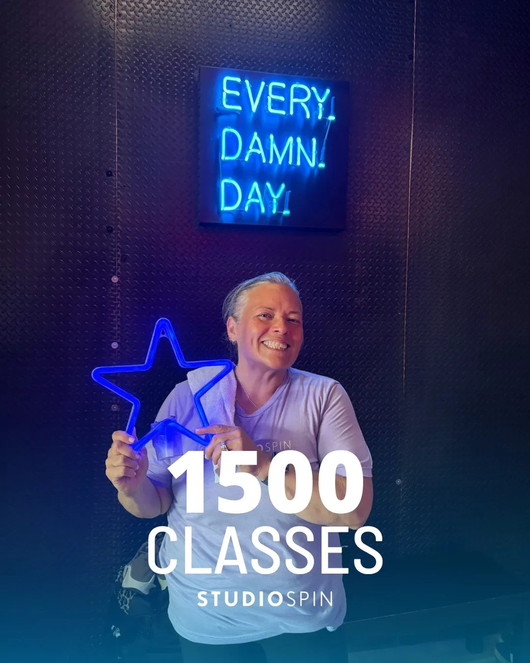 A Studio Spin member celebrating 1,500 classes under the Every Damn Day neon sign.